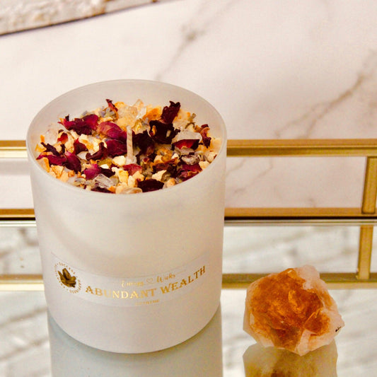 6oz soy candle with one wick, housed in a white container next to citrine quartz cluster on marble background. Decorated with citrine, clear quartz, dried rose petals, and lavender. Infused with a grapefruit and mangosteen aromatherapy fragrance, it is part of the Ultimate Abundant Wealth Crystal Candle collection, created to inspire prosperity and abundance.