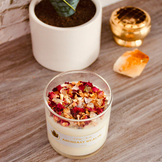 6oz soy candle with one wick, housed in a clear container on a decorative background. Decorated with citrine, clear quartz, dried rose petals, and lavender. Infused with a grapefruit and mangosteen aromatherapy fragrance, it is part of the Ultimate Abundant Wealth Crystal Candle collection, created to inspire prosperity and abundance.