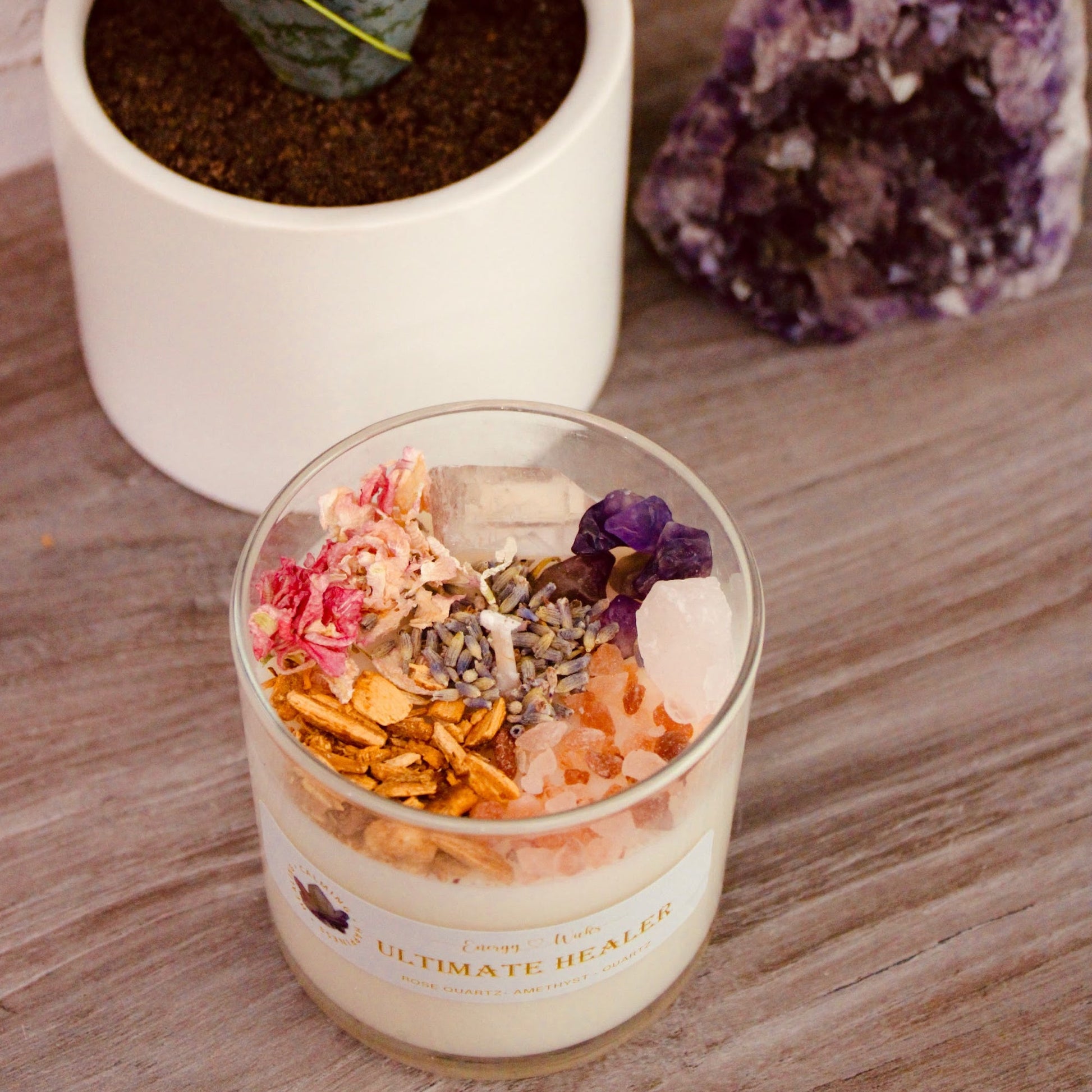 Ultimate Healer Crystal Candle in a simple clear jar container, adorned with rose quartz and amethyst stones, designed to promote purity, peace, and love. Also empowered with lavender, rose, palo santo, and more. Bath and Body Works Pure Paradise replica scent. Available in three sizes: 1 wick/6oz, 2 wicks/10oz, and 3 wicks/16oz.