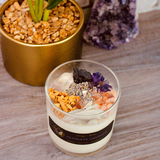 6oz soy candle with one wick, nestled in a clear glass container on tabletop. Adorned with dried lavender, Black Tourmaline, Amethyst, and clear Quartz crystals, it carries a Basil, Mint, and Sage fragrance. Part of the Ultimate Smudger crystal candle collection, designed to cleanse spaces and clear negative energies.