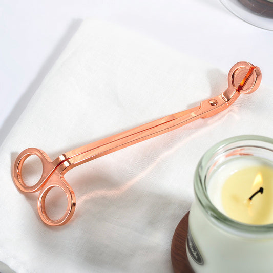 Rose gold candle snuffer next to a lit candle on a white surface